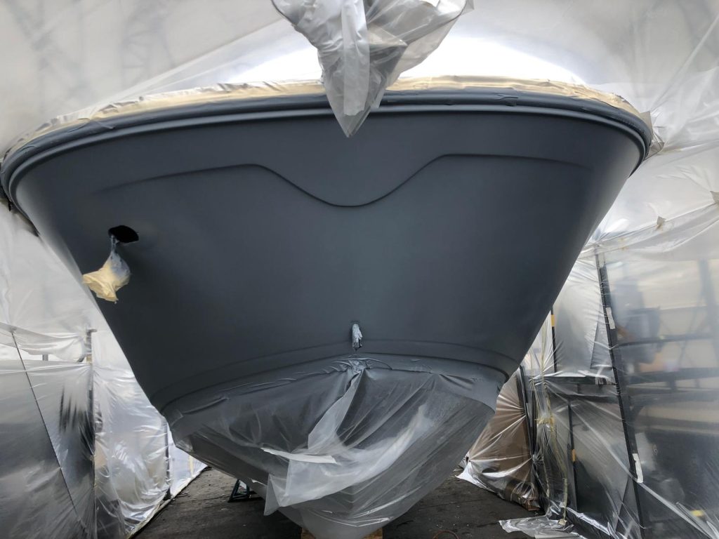 Boat bow sanded and primed in gray inside a plastic-tented spray booth