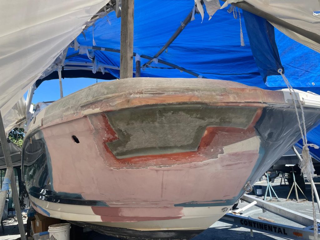 Fiberglass repair in progress on a boat bow, hull faired and re-glassed under a work tent