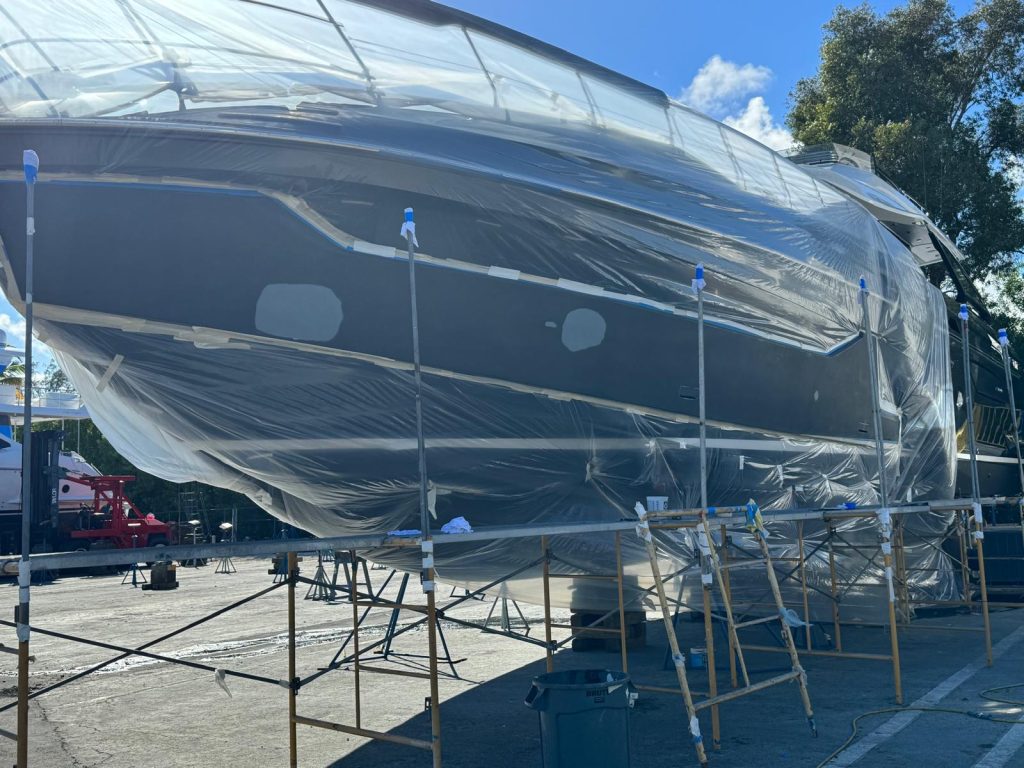 Dark gray yacht hull masked on scaffolding with spot primer repairs during paint refinishing