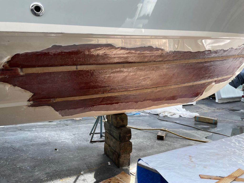 Hull strakes rebuilt with fiberglass and red fairing compound during structural repair