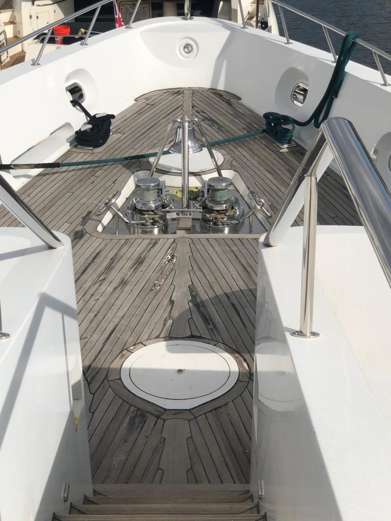 Yacht foredeck with teak decking, polished anchor windlasses and freshly refinished white fiberglass