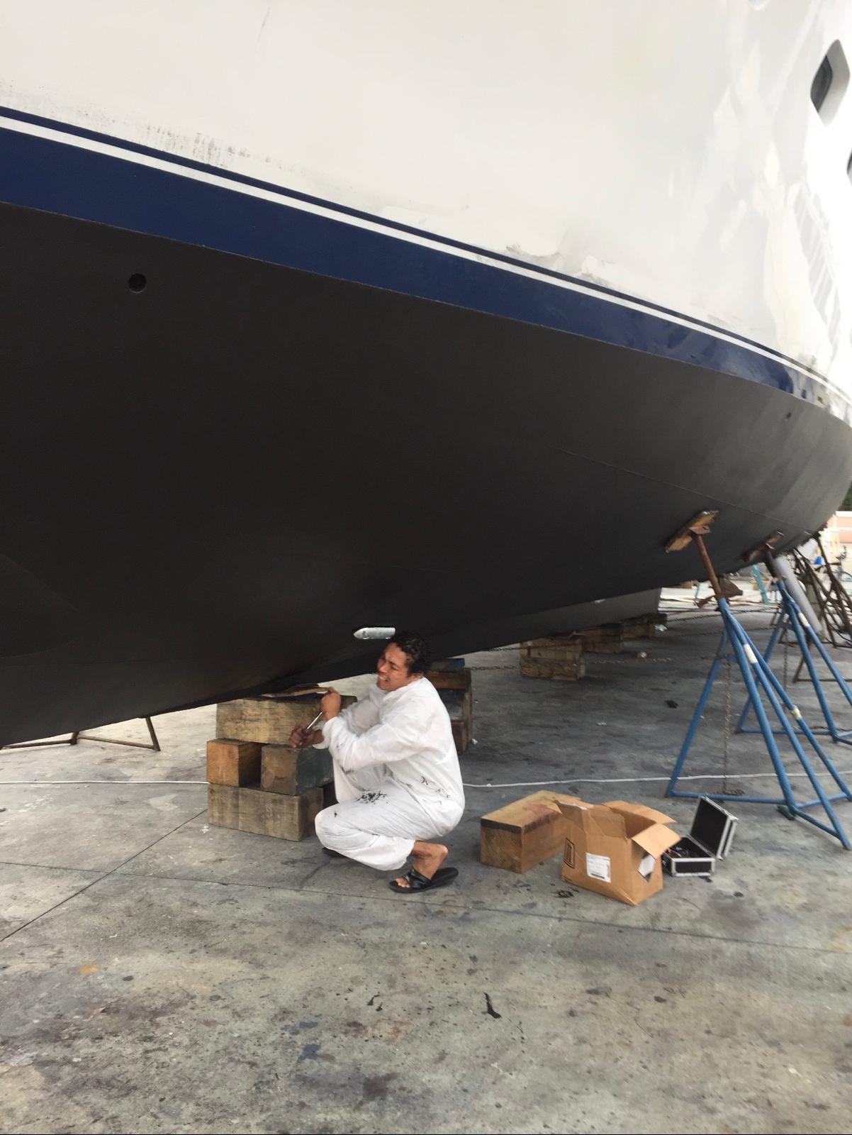 Freshly applied black bottom paint on a yacht hull with a crew member touching up at the jack stands
